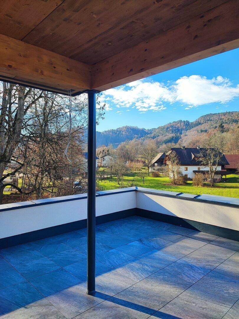 Sonnige Terrasse mit Fliesenboden und Panoramablick auf die umliegende Natur und Häuser.