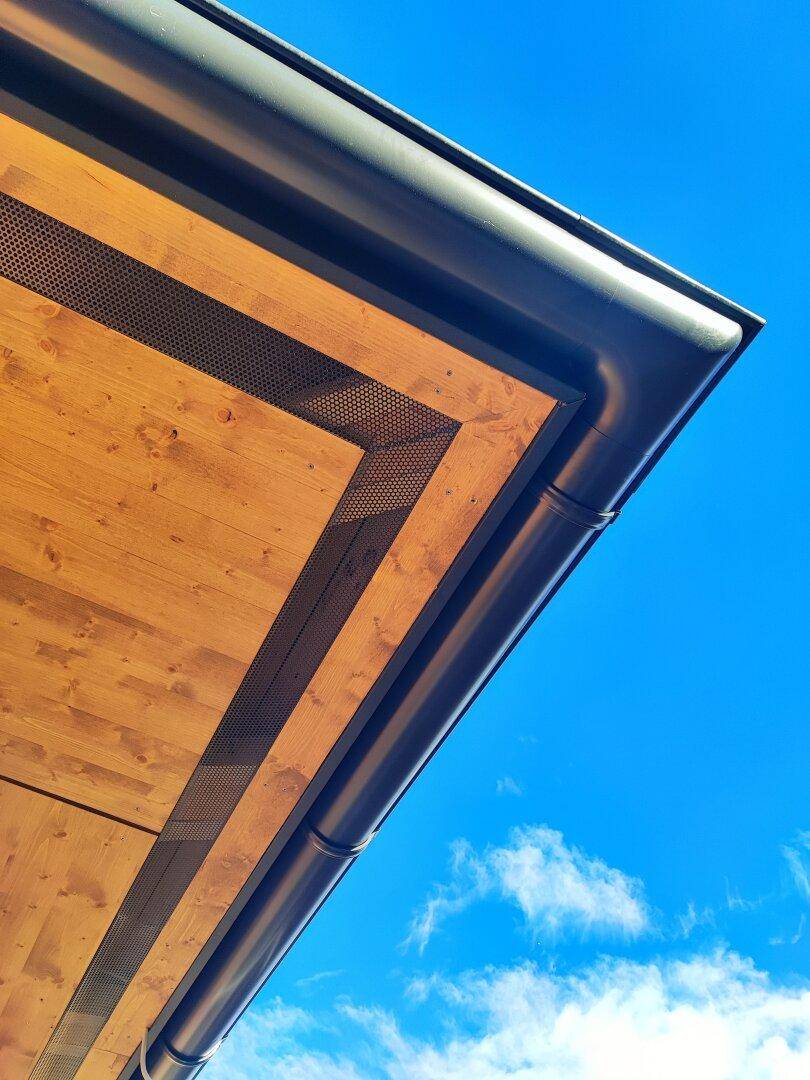Detailansicht des modernen Dachüberstands mit Holzverkleidung und Regenrinne unter blauem Himmel.