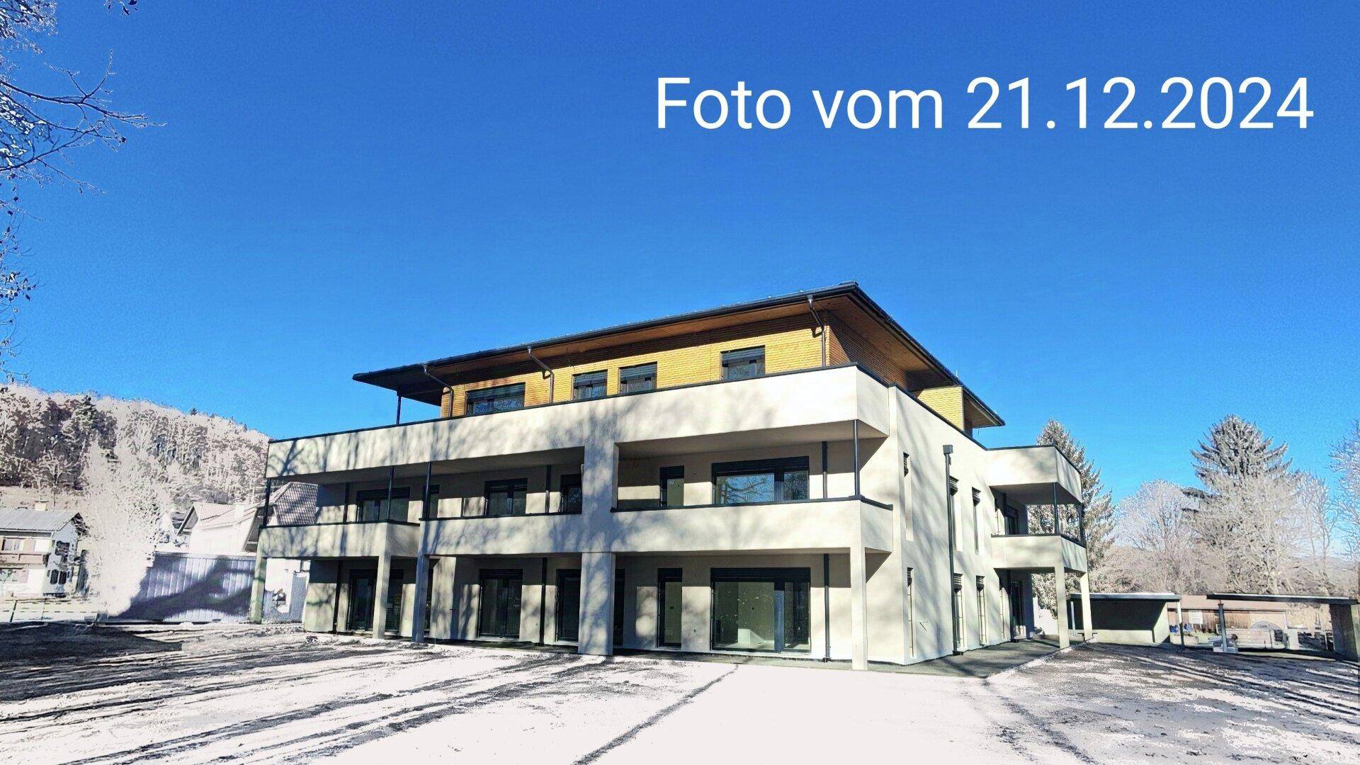 Modernes Mehrfamilienhaus mit Balkonen und Holzverkleidung, umgeben von winterlicher Landschaft.