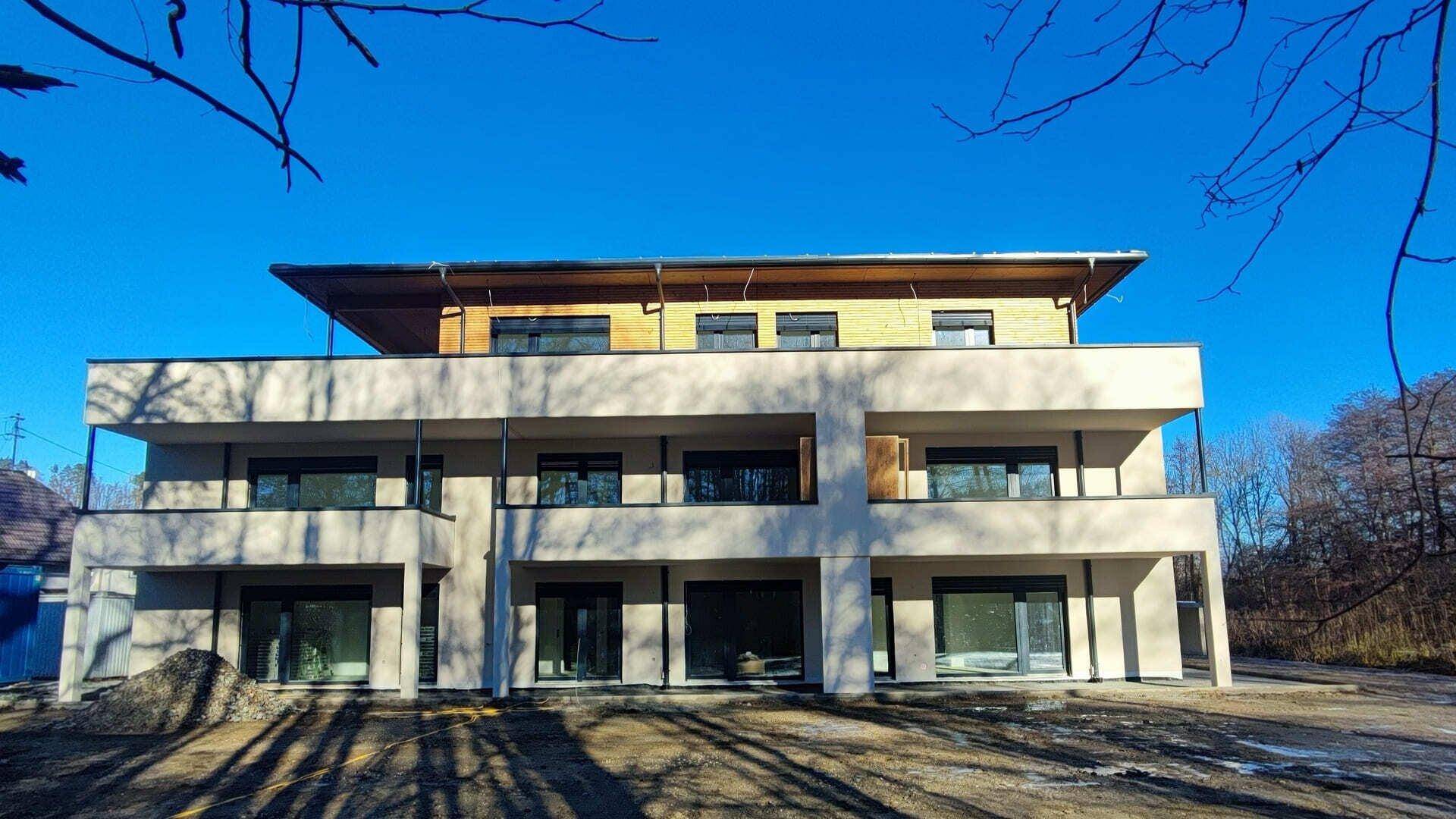 Neubau-Fassade mit modernen Balkonen und großen Fensterfronten unter klarem Winterhimmel.