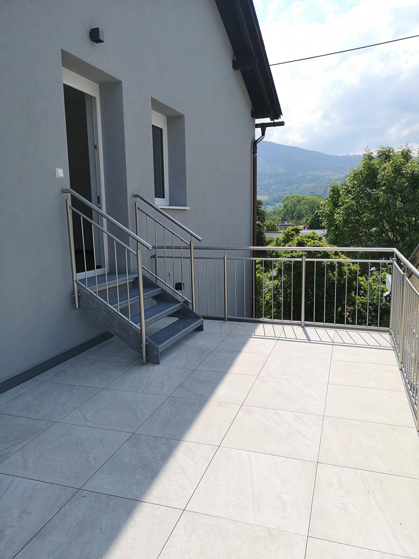 Moderne Terrasse mit hellen Fliesen, Edelstahlgeländer und weitem Blick auf die umliegende Berglandschaft.