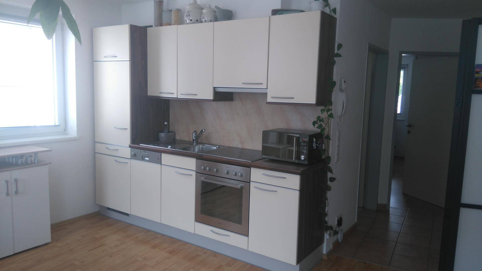 Funktionale Einbauküche mit hellen Fronten, integrierten Geräten und Fenster.
