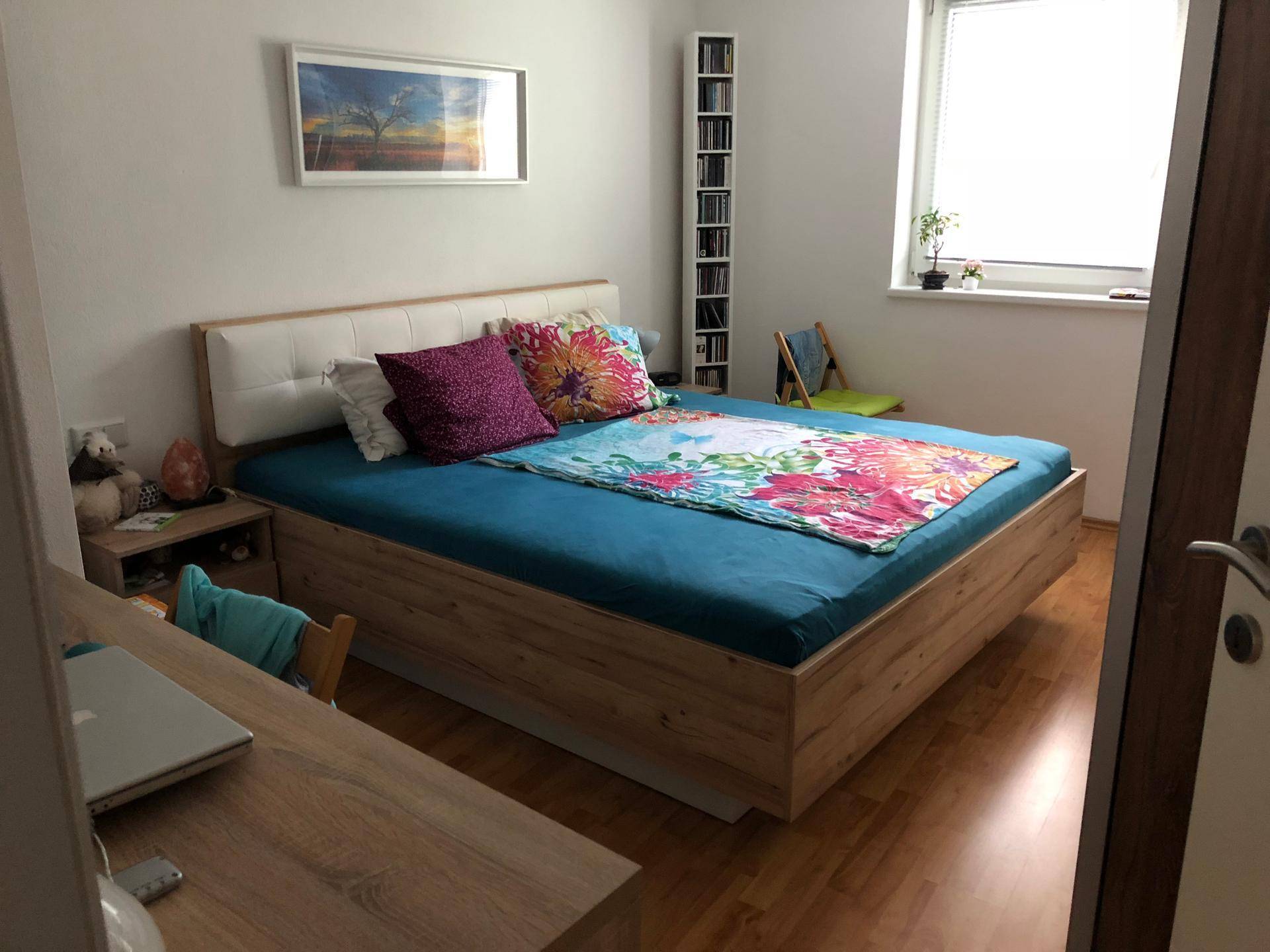 Helles Schlafzimmer mit Holzbett, Schreibtisch und Fenster für natürliches Licht.