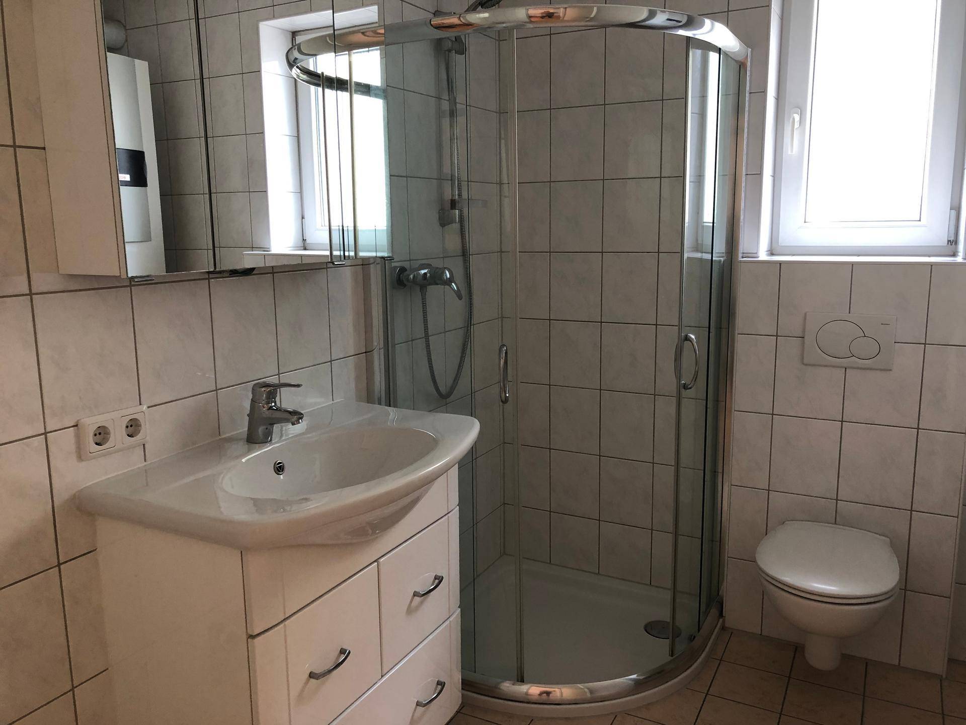 Modernes Badezimmer mit Duschkabine, Waschbecken und WC, hell gefliest.