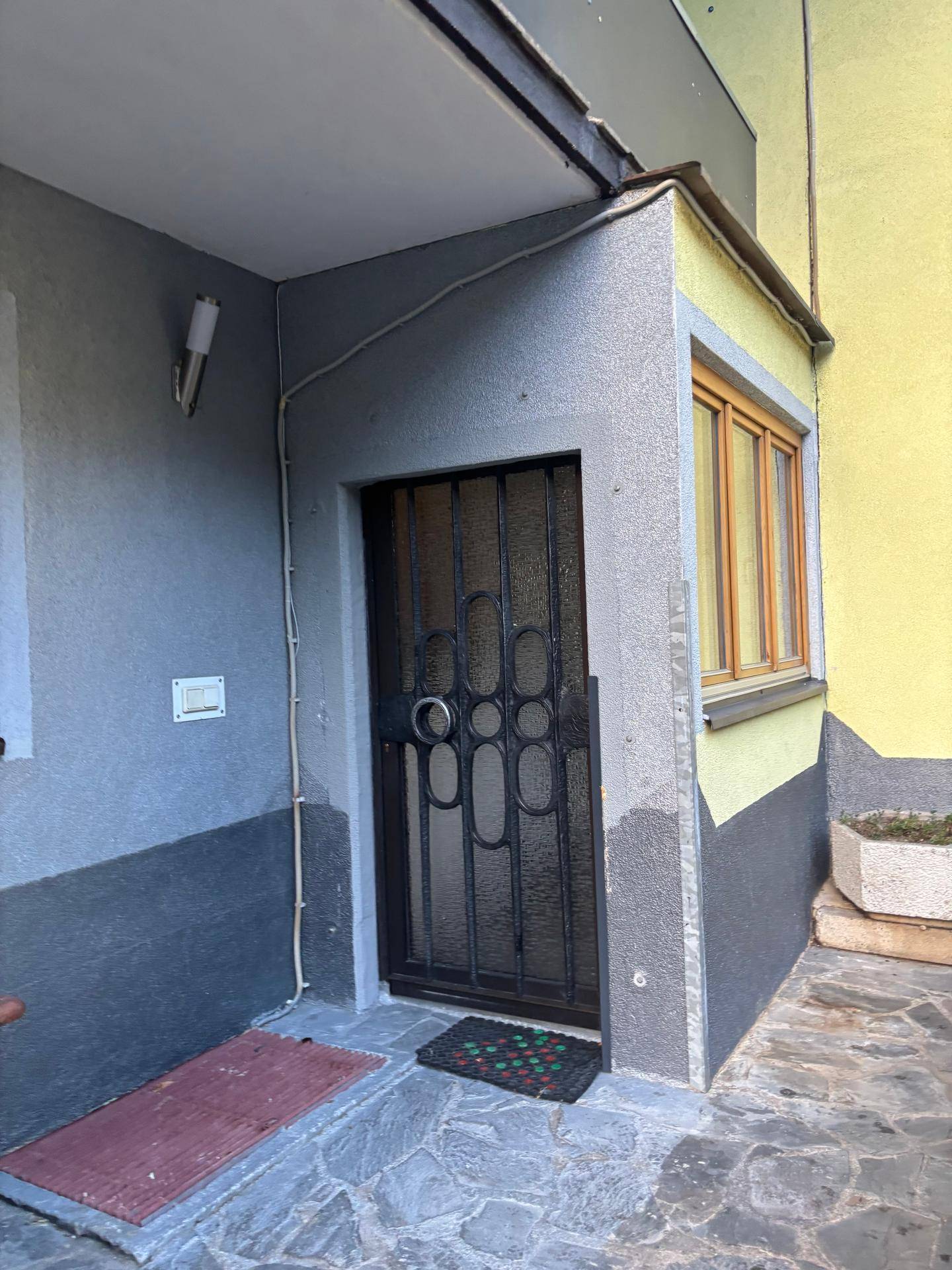 Eingangsbereich des Gebäudes mit dunkler Sicherheitstür und kleinem Fenster.