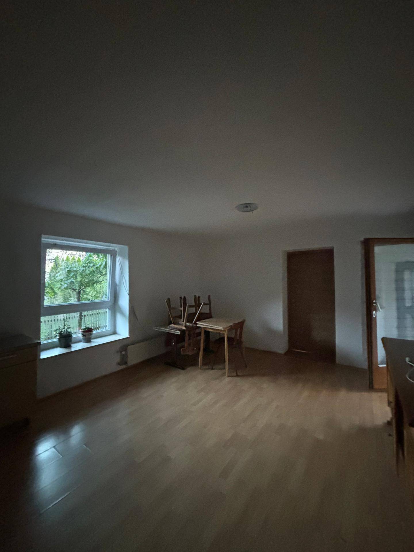 Geräumiger Wohnraum mit Holzboden, Fenster und einem kleinen Esstisch.