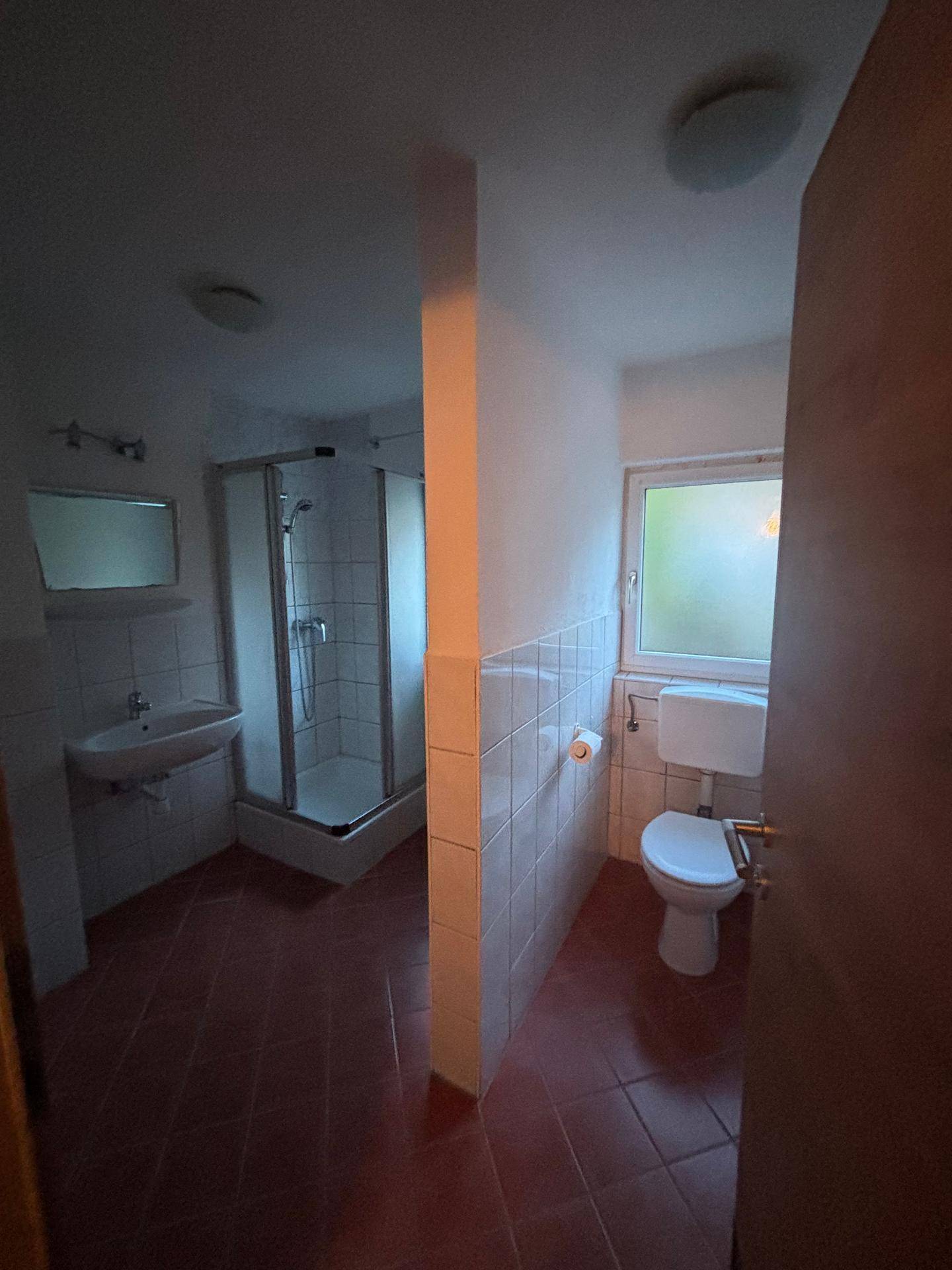 Badezimmer mit Fliesenboden, Duschkabine, Waschbecken und Toilette.