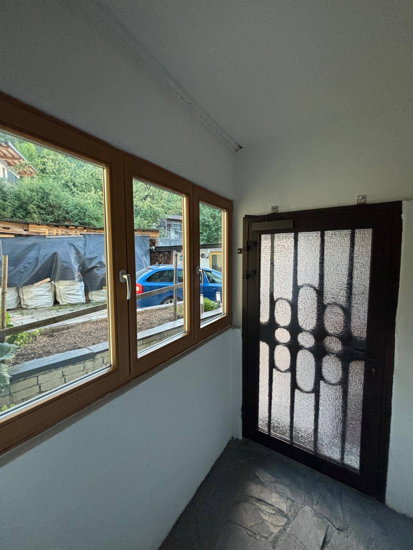 Innenansicht eines Eingangsbereichs mit Fenster und dunkler Sicherheitstür.