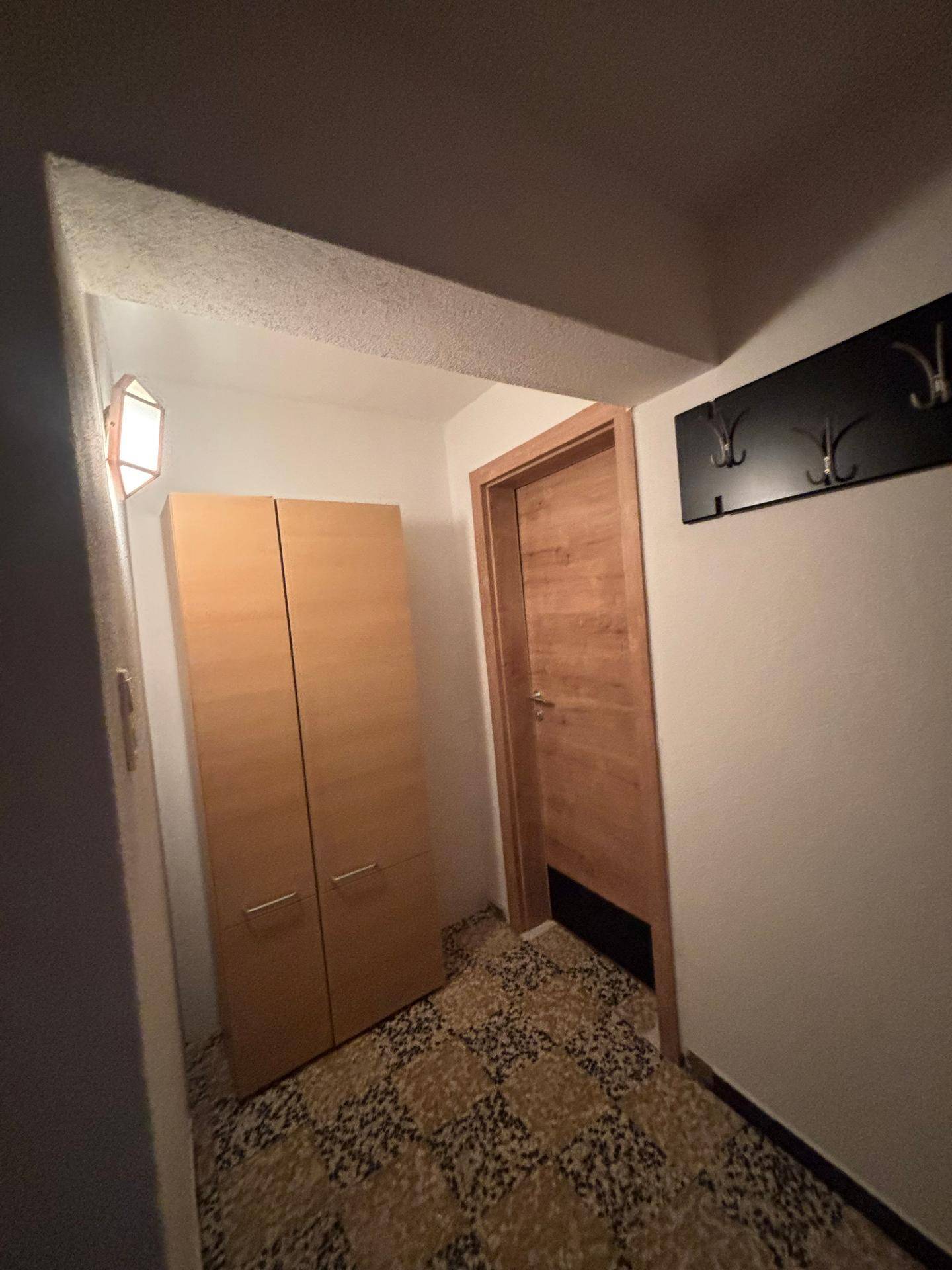 Flur mit gemustertem Fliesenboden und einem Holzschrank.