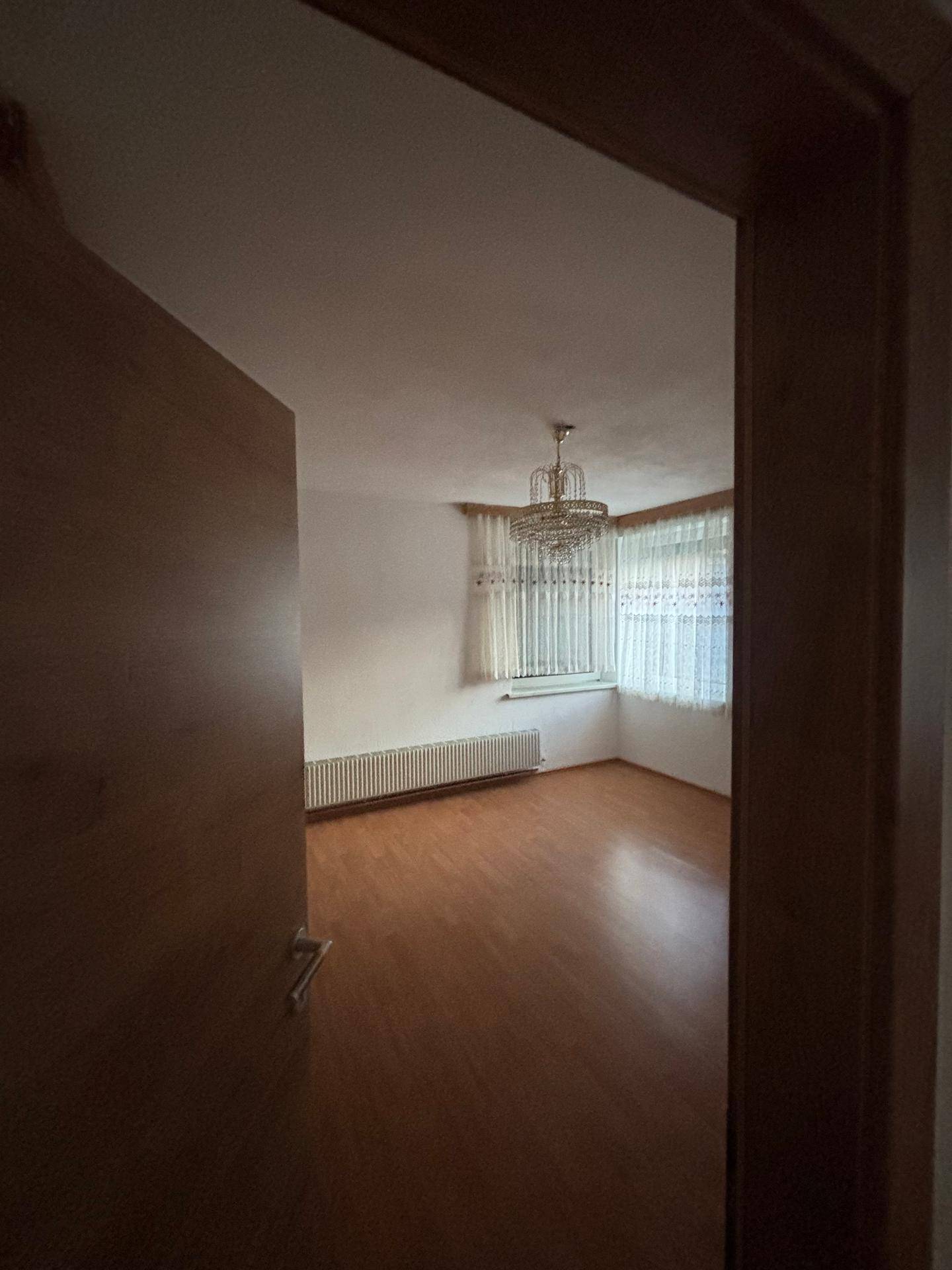 Blick in ein Zimmer mit Laminatboden, Heizkörper und einem eleganten Kronleuchter.