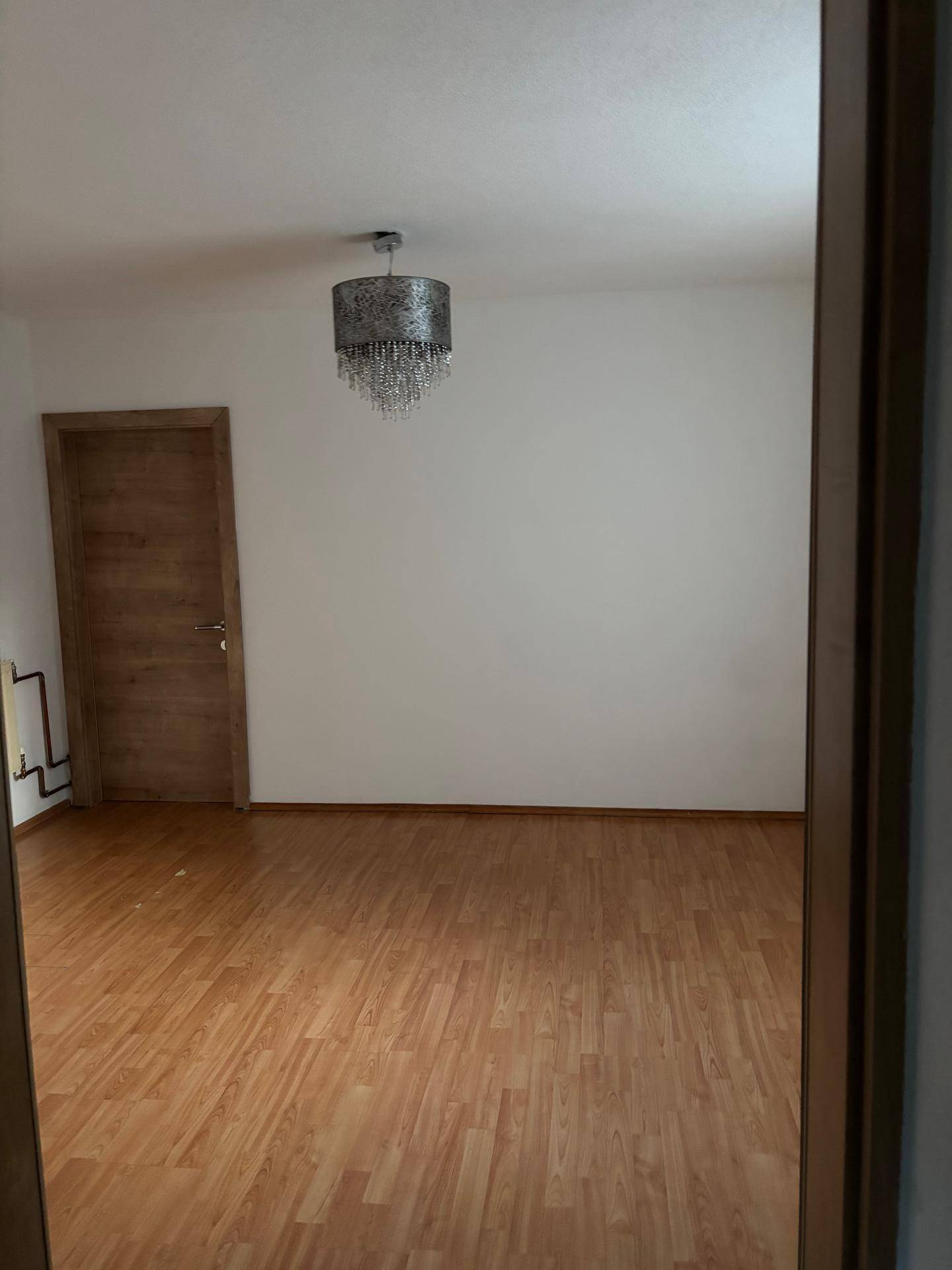 Leeres Zimmer mit Laminatboden und einer modernen Deckenleuchte.