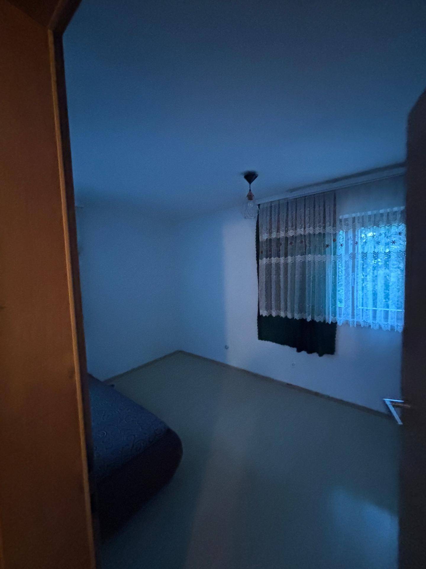 Schwach beleuchtetes Schlafzimmer mit einem Bett und einem Fenster mit Vorhängen.