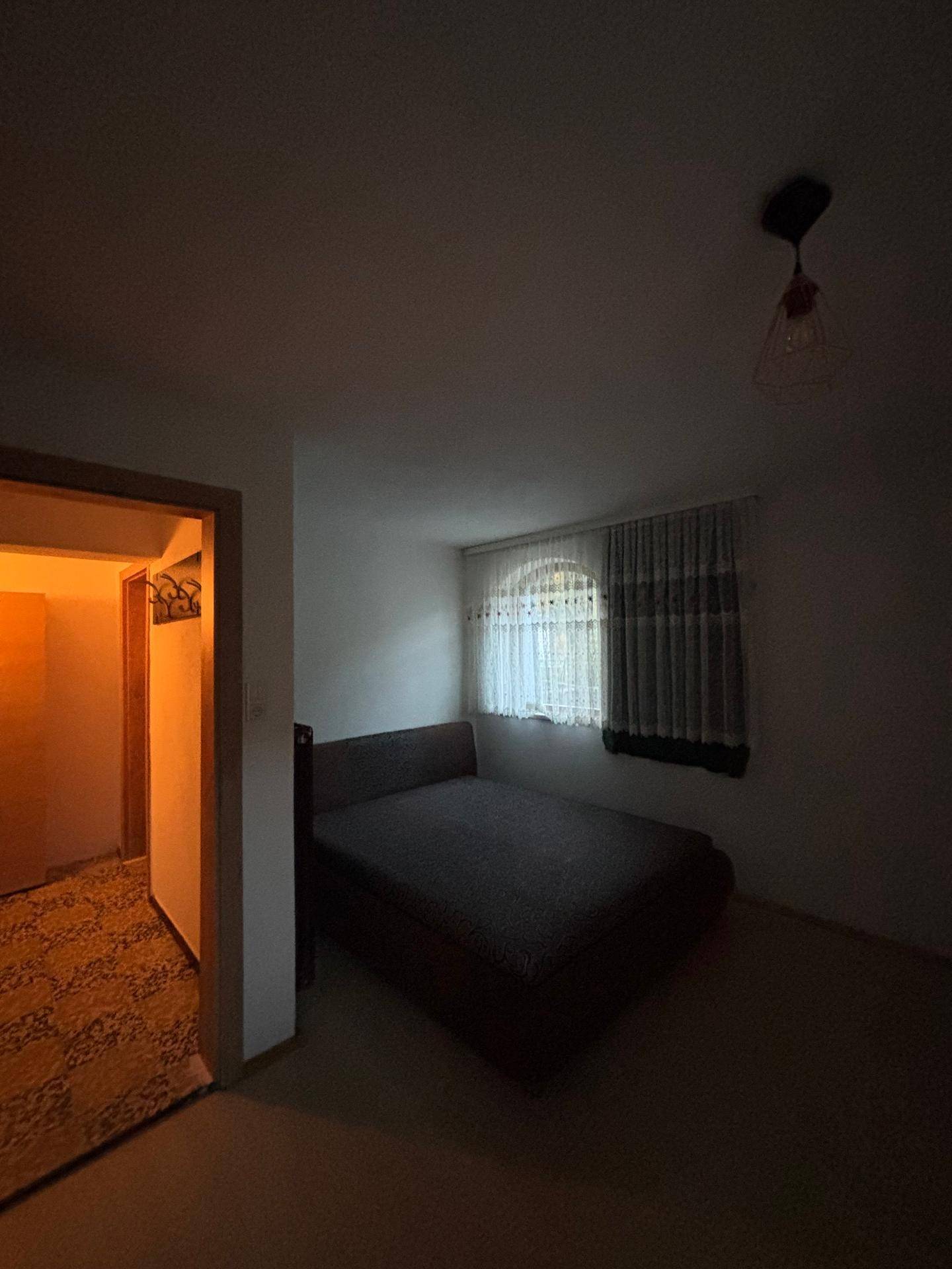 Schlafzimmer mit Bett und Zugang zum Flur, beleuchtet durch ein Fenster.