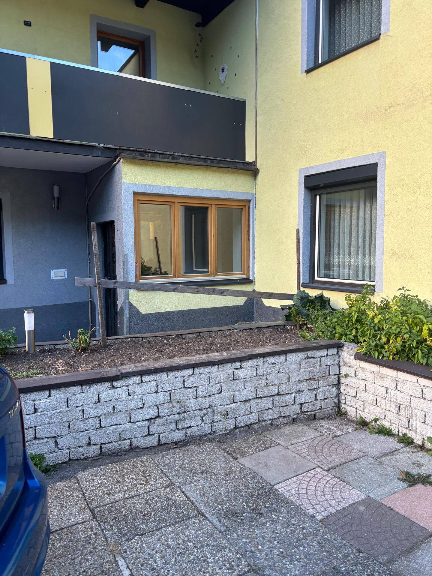 Detailansicht der Gebäudefassade mit kleinem Gartenbeet und gepflastertem Bereich.