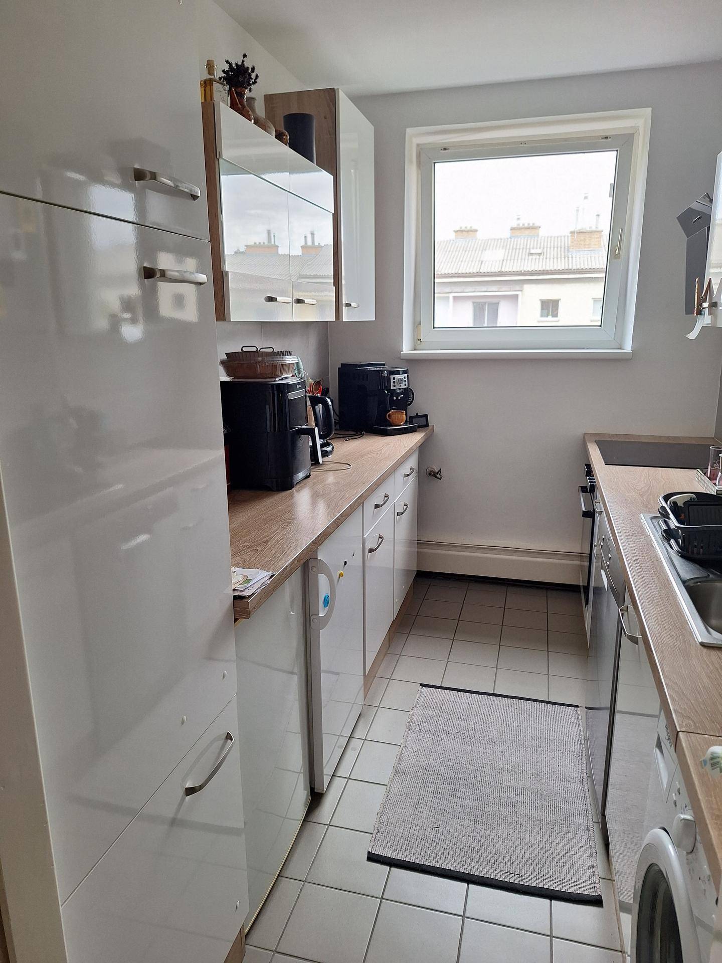 Kleine Küche mit weißen Hochglanzschränken, Holz-Arbeitsplatte und Fenster.