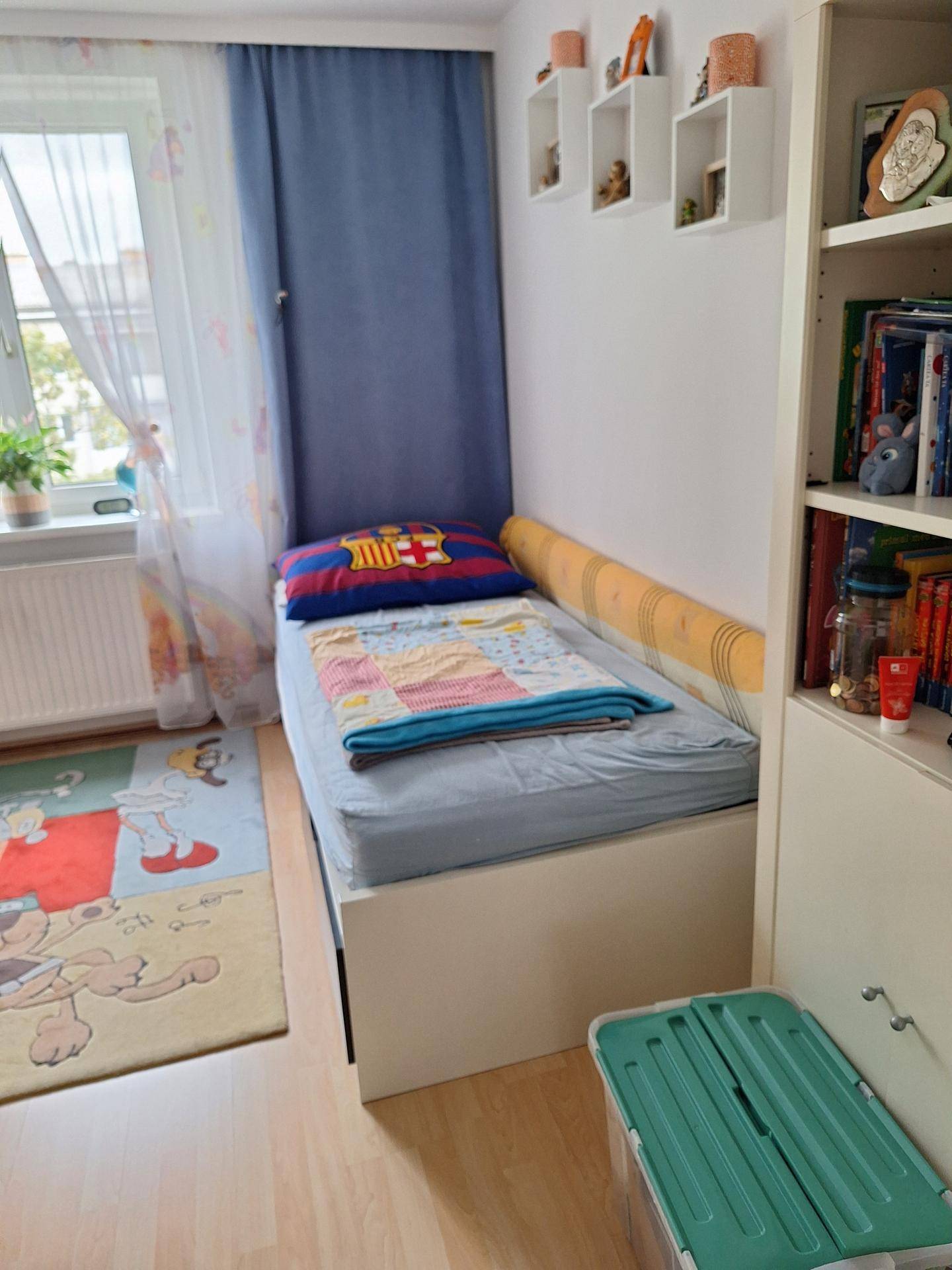 Kinderzimmer mit Einzelbett, farbenfrohem Teppich und Fenster für natürliches Licht.