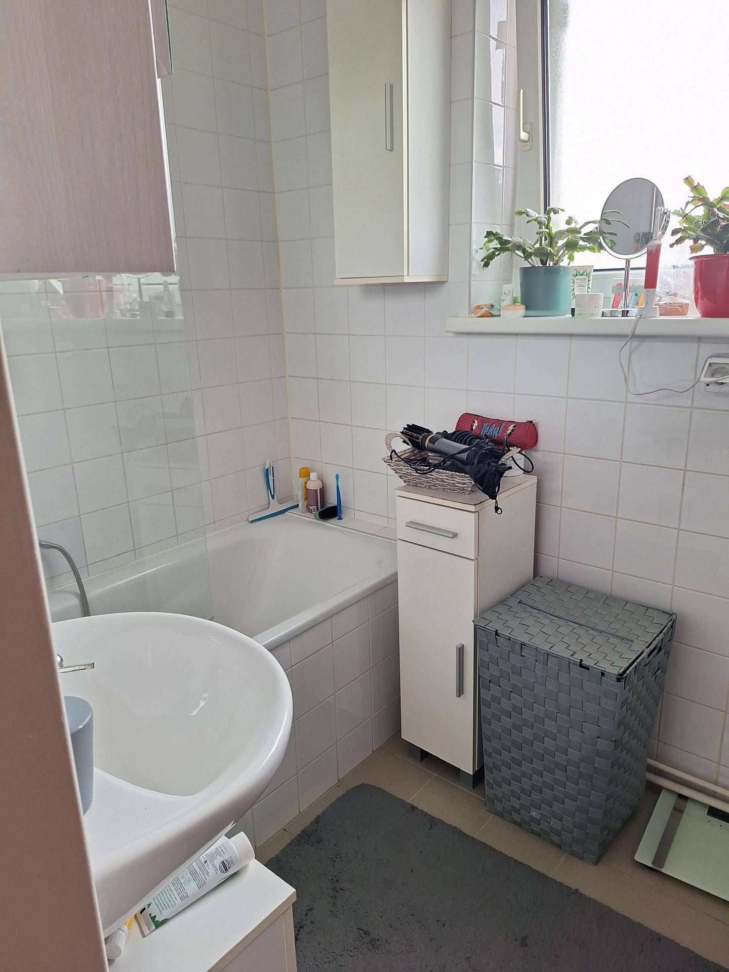 Badezimmer mit Badewanne, Waschbecken und Fenster, komplett gefliest in Weiß.