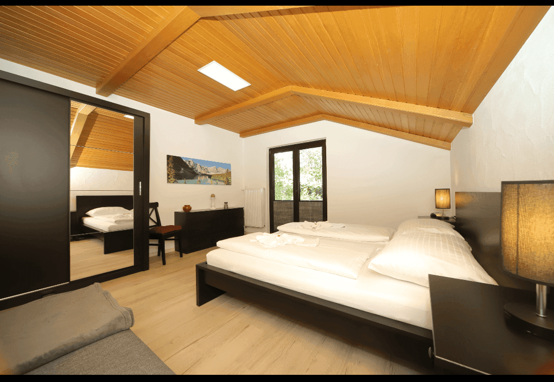 Gemütliches Schlafzimmer mit Holzbalkendecke, Doppelbett und Zugang zum Balkon.
