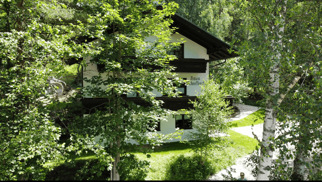 Haus im Grünen, umgeben von hohen Bäumen und üppiger Vegetation.