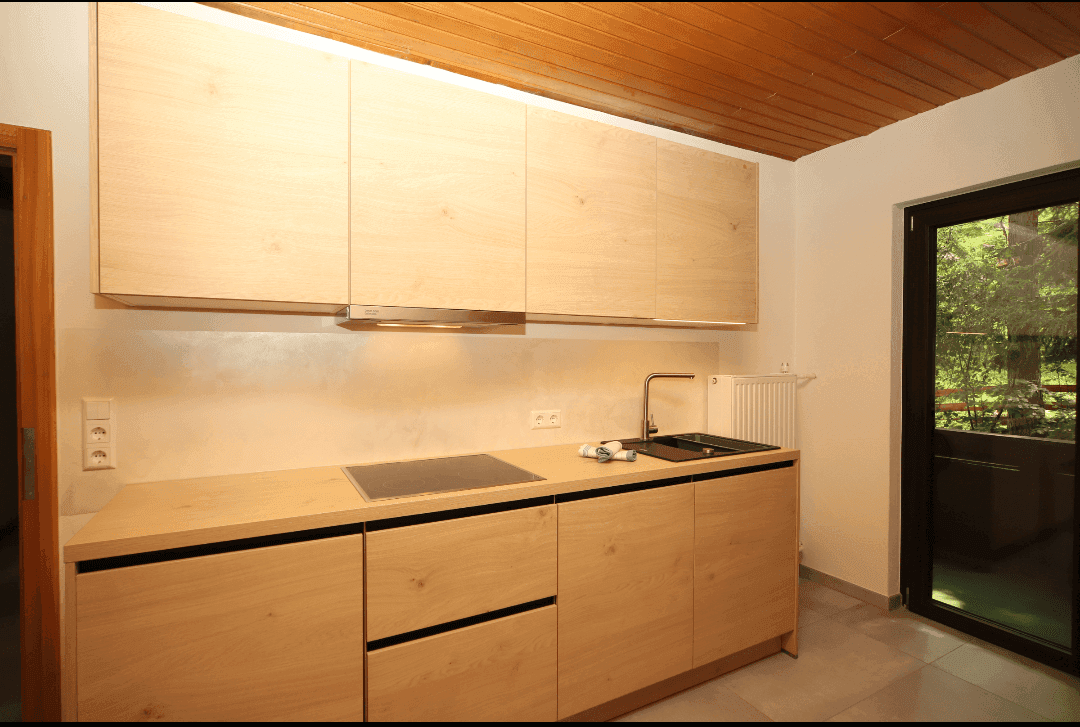 Helle Einbauküche mit Holzfronten, Induktionskochfeld und Zugang zum Balkon.