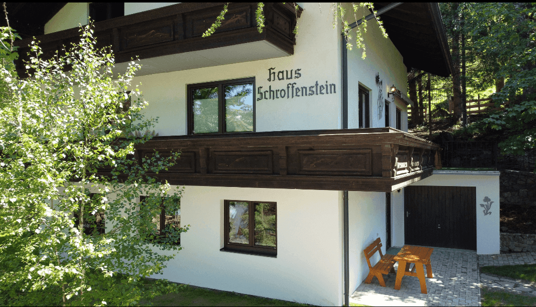 Traditionelles Haus mit Holzbalkonen und Garage, umgeben von grüner Natur.