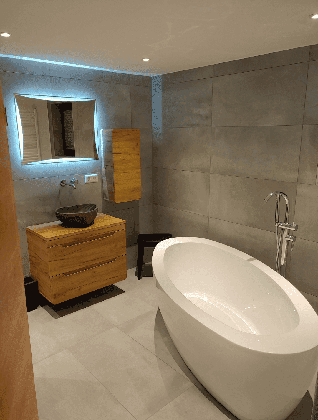 Modernes Badezimmer mit freistehender Badewanne, Holzwaschtisch und beleuchtetem Spiegel.