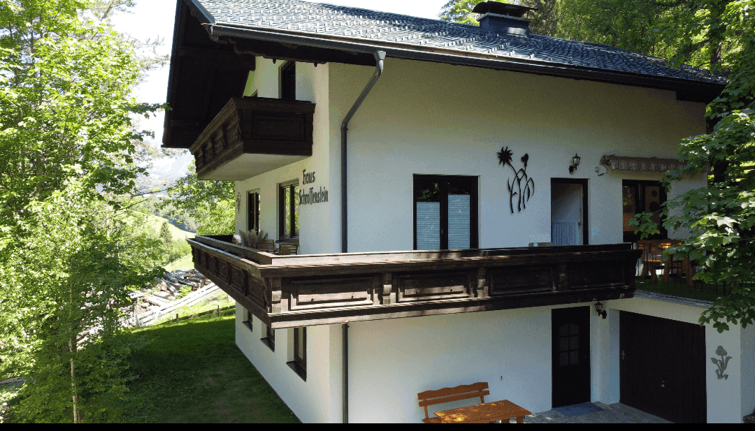 Haus im alpinen Stil mit Holzbalkonen und Blick auf die umliegende Berglandschaft.