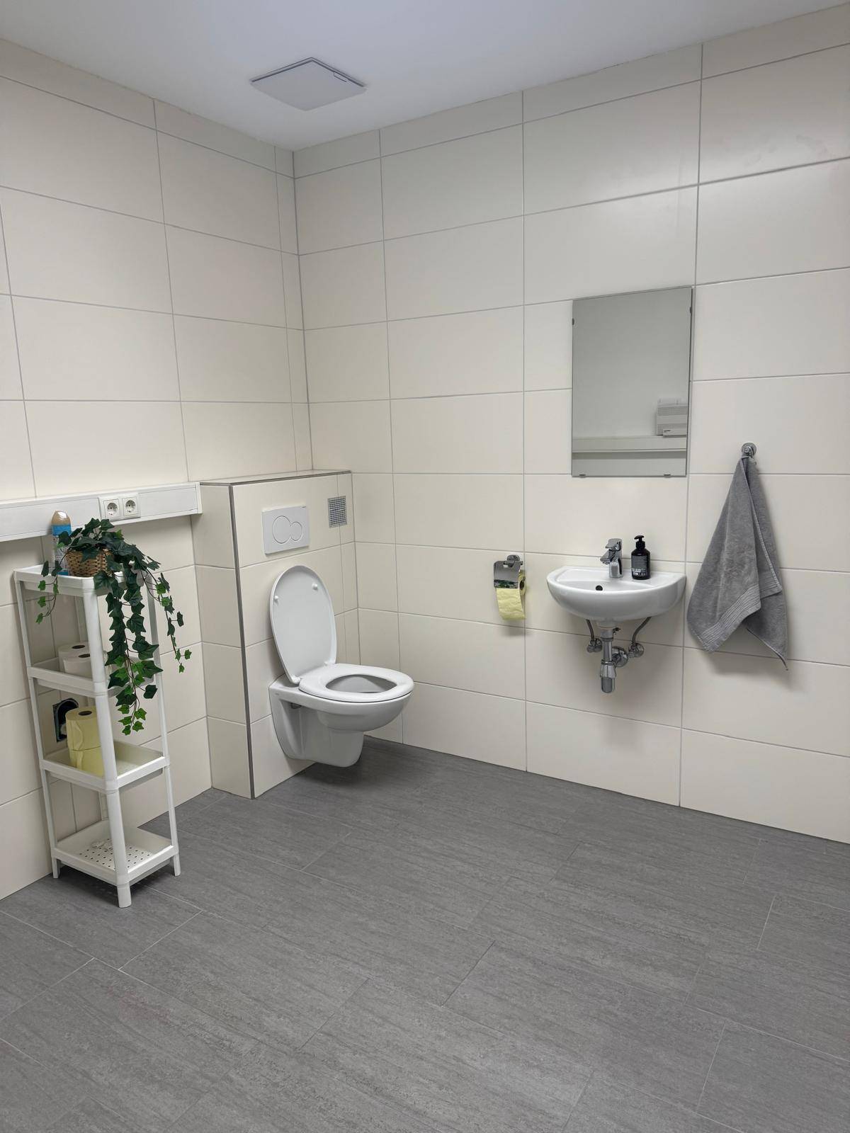 Modernes WC mit Wand-WC, kleinem Waschbecken und weißen Fliesen an den Wänden.