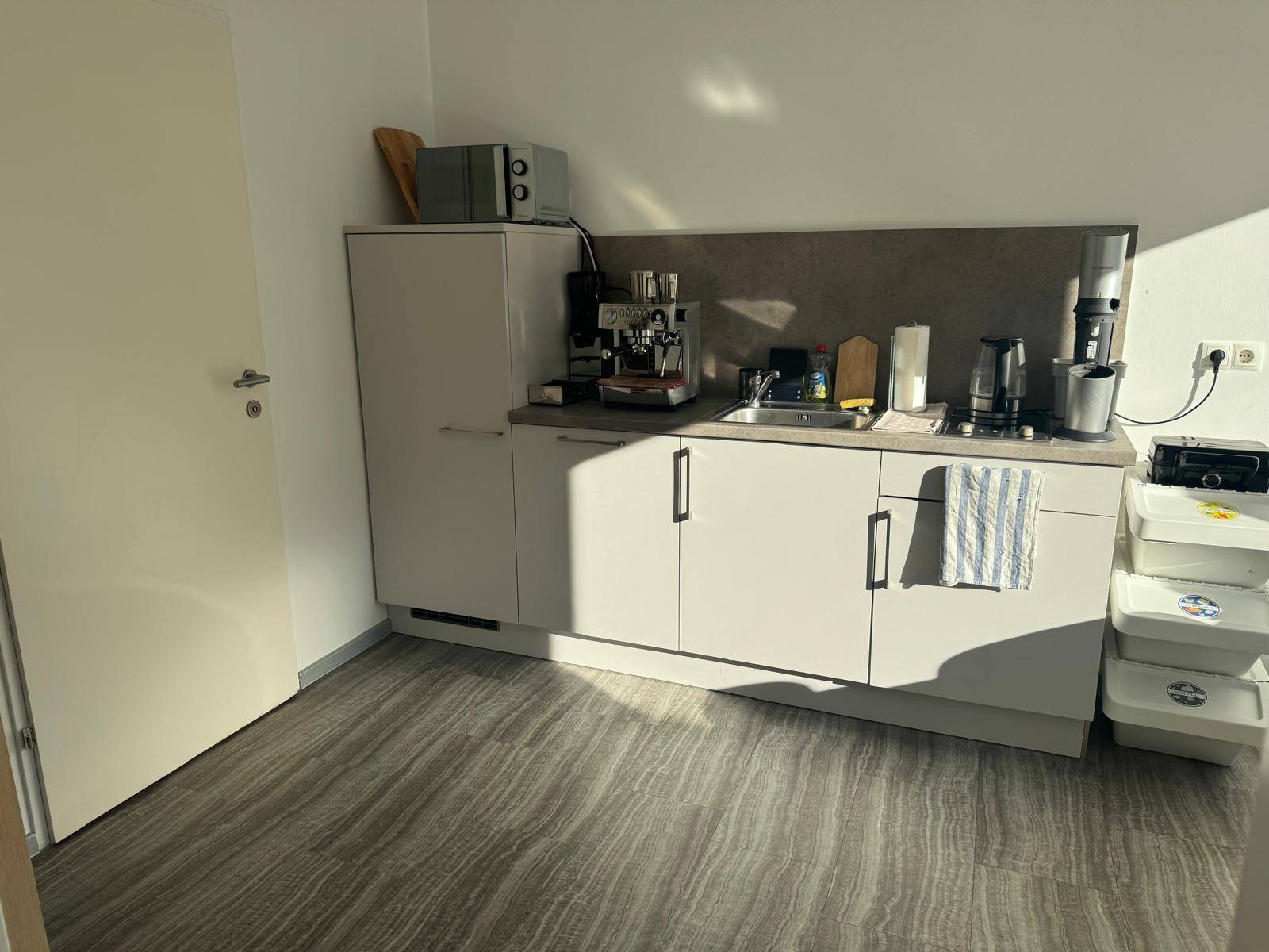 Kompakte Küchenzeile mit Spüle, Mikrowelle und Kaffeemaschine, in einem hellen Raum.