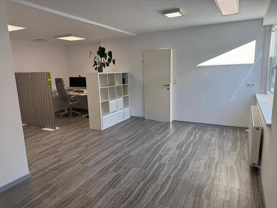 Offener Bürobereich mit Vinylboden, weißen Wänden und einem Arbeitsplatz im Hintergrund.