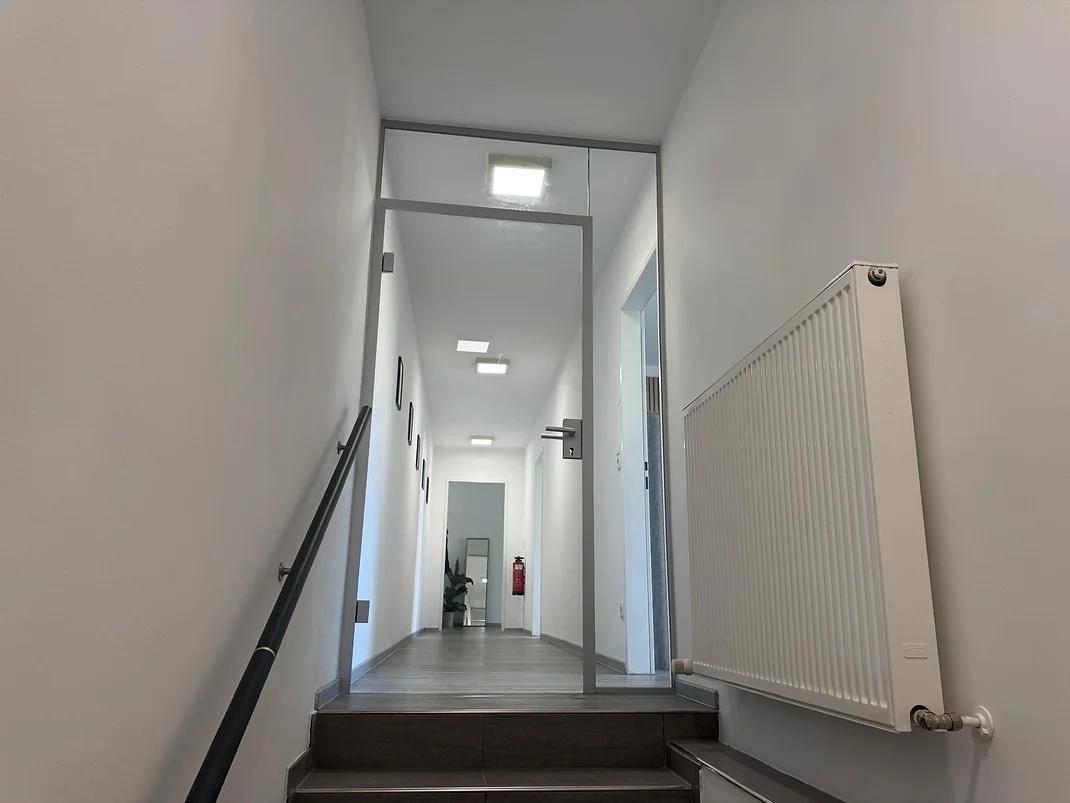 Heller Flur mit Treppenaufgang, Glaswand und Heizkörper, führt zu weiteren Räumen.