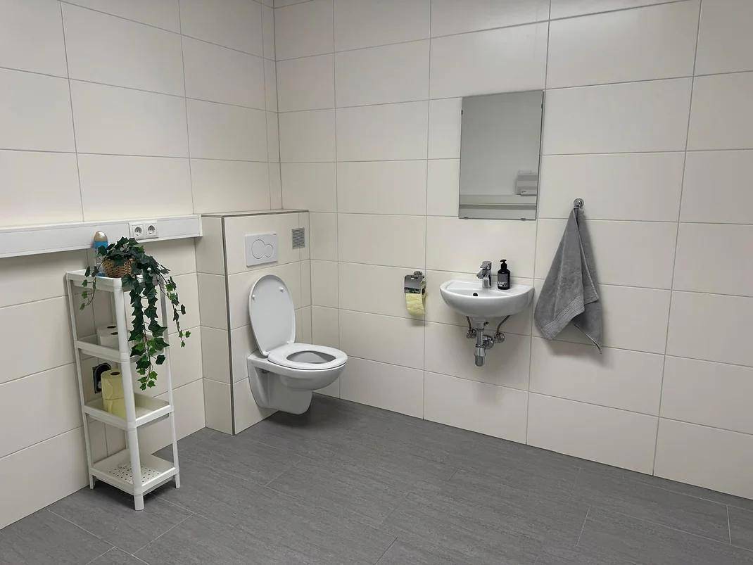 Modernes WC mit Wand-WC, kleinem Waschbecken und weißen Fliesen an den Wänden.