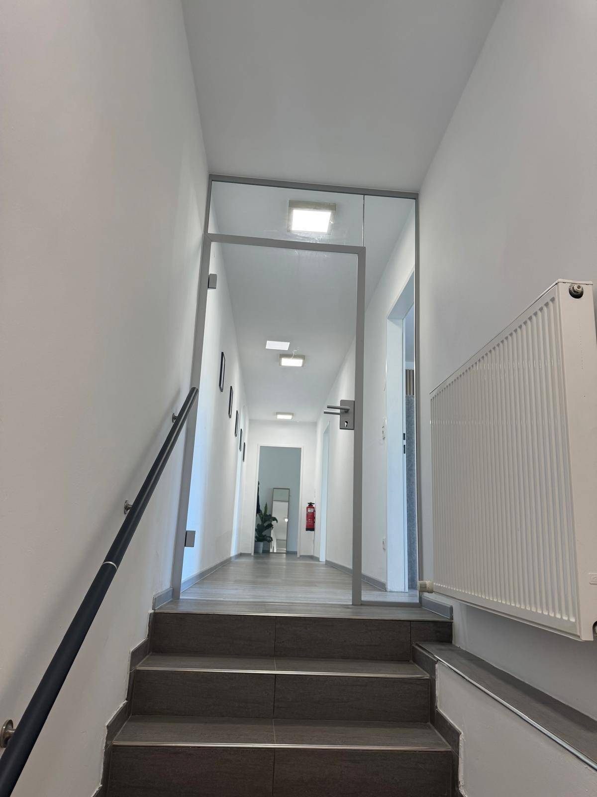Heller Flur mit Treppenaufgang, Glaswand und Heizkörper, führt zu weiteren Räumen.