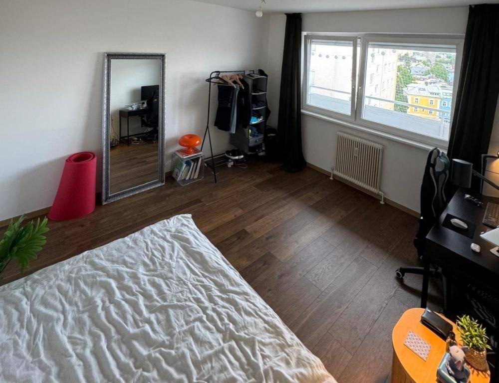 Geräumiges Schlafzimmer mit Holzboden, großem Fenster und einem praktischen Arbeitsbereich.