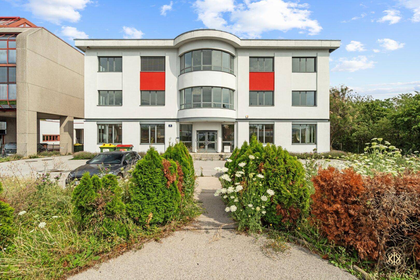 Modernes Bürogebäude mit geschwungener Fassade, roten Akzenten und gepflegter Grünanlage davor.