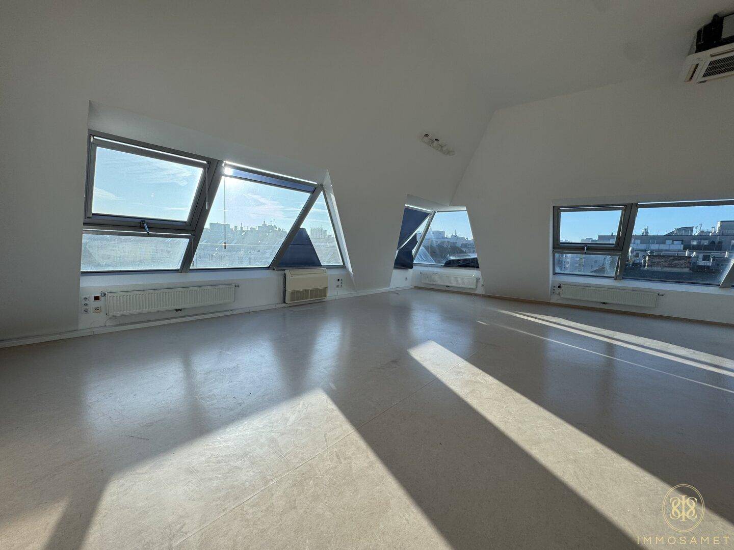 Großer, leerer Dachgeschossraum mit vielen Fenstern, die viel natürliches Licht hereinlassen und eine weite Aussicht bieten.