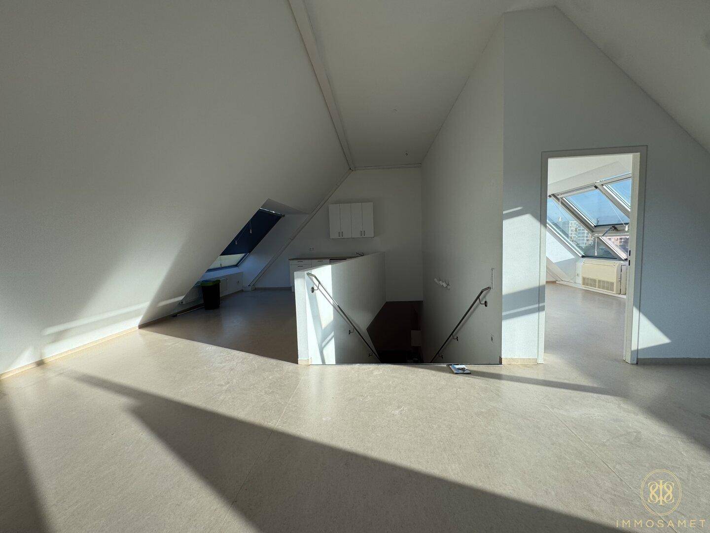 Heller Dachgeschossraum mit Treppenabgang und Blick auf weitere Räume durch eine Türöffnung.