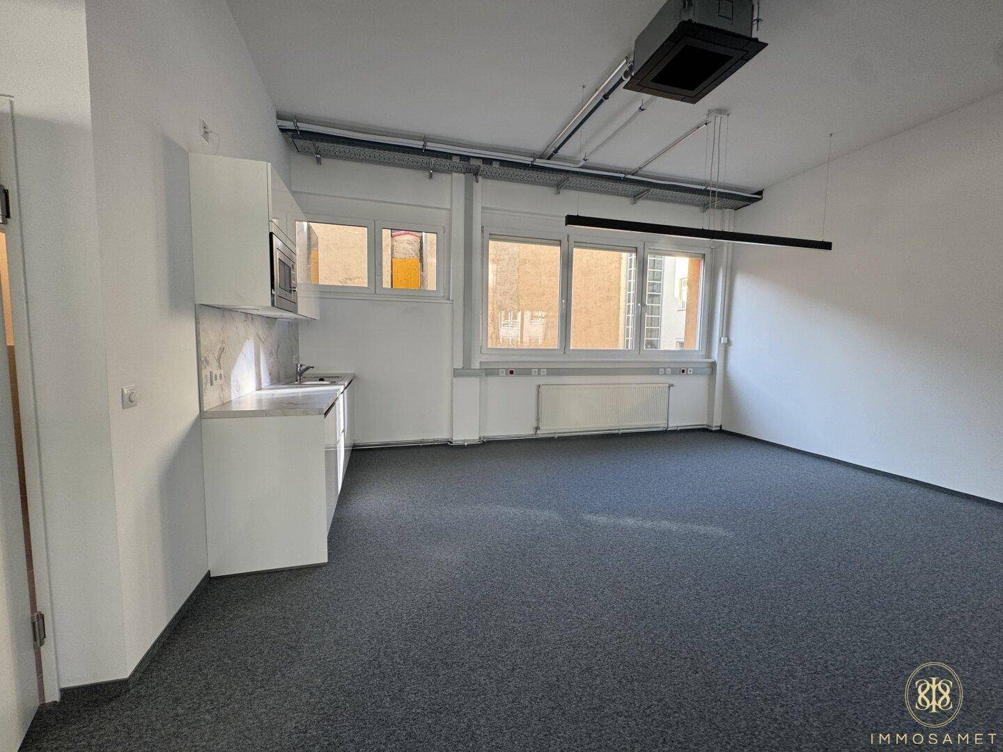 Moderne Küchenzeile mit weißen Hochglanzschränken, Marmor-Optik-Rückwand und integrierter Mikrowelle in einem hellen Bürobereich.