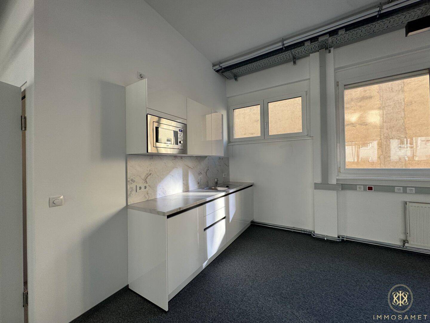 Kompakte Küchenzeile mit weißen Schränken, Spülbecken und Mikrowelle, praktisch in den Büroraum integriert für schnelle Pausen.