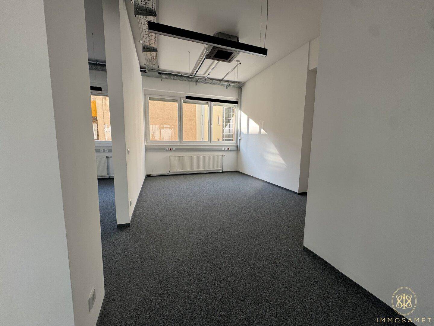 Flexibler Bürobereich mit Trennwänden, grauem Teppichboden und großen Fenstern, die eine helle und anpassbare Arbeitsumgebung schaffen.