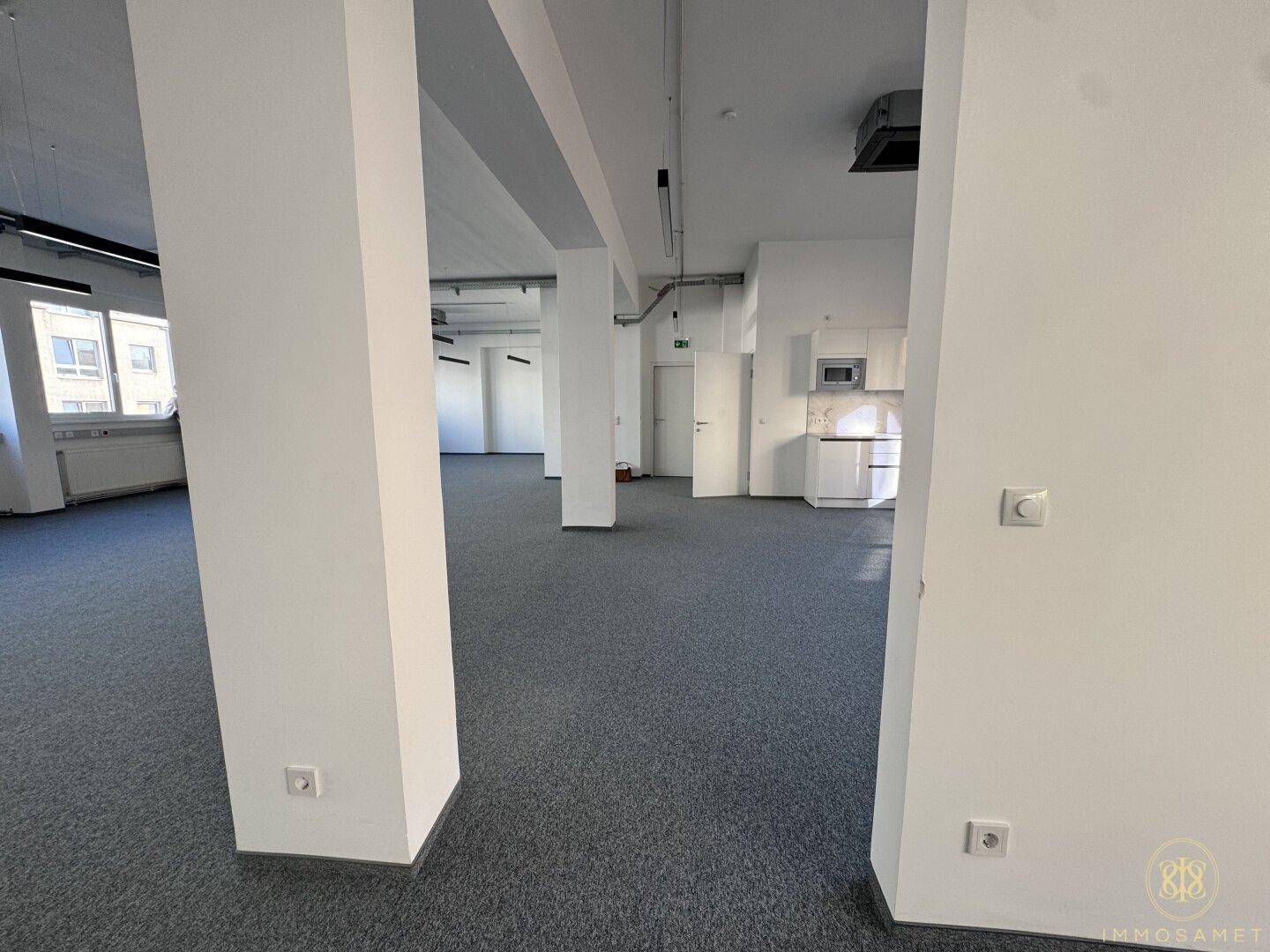 Großzügiger Büroraum mit Säulen, integrierter Küchenzeile und Teppichboden, ideal für ein offenes Bürokonzept mit viel Tageslicht.