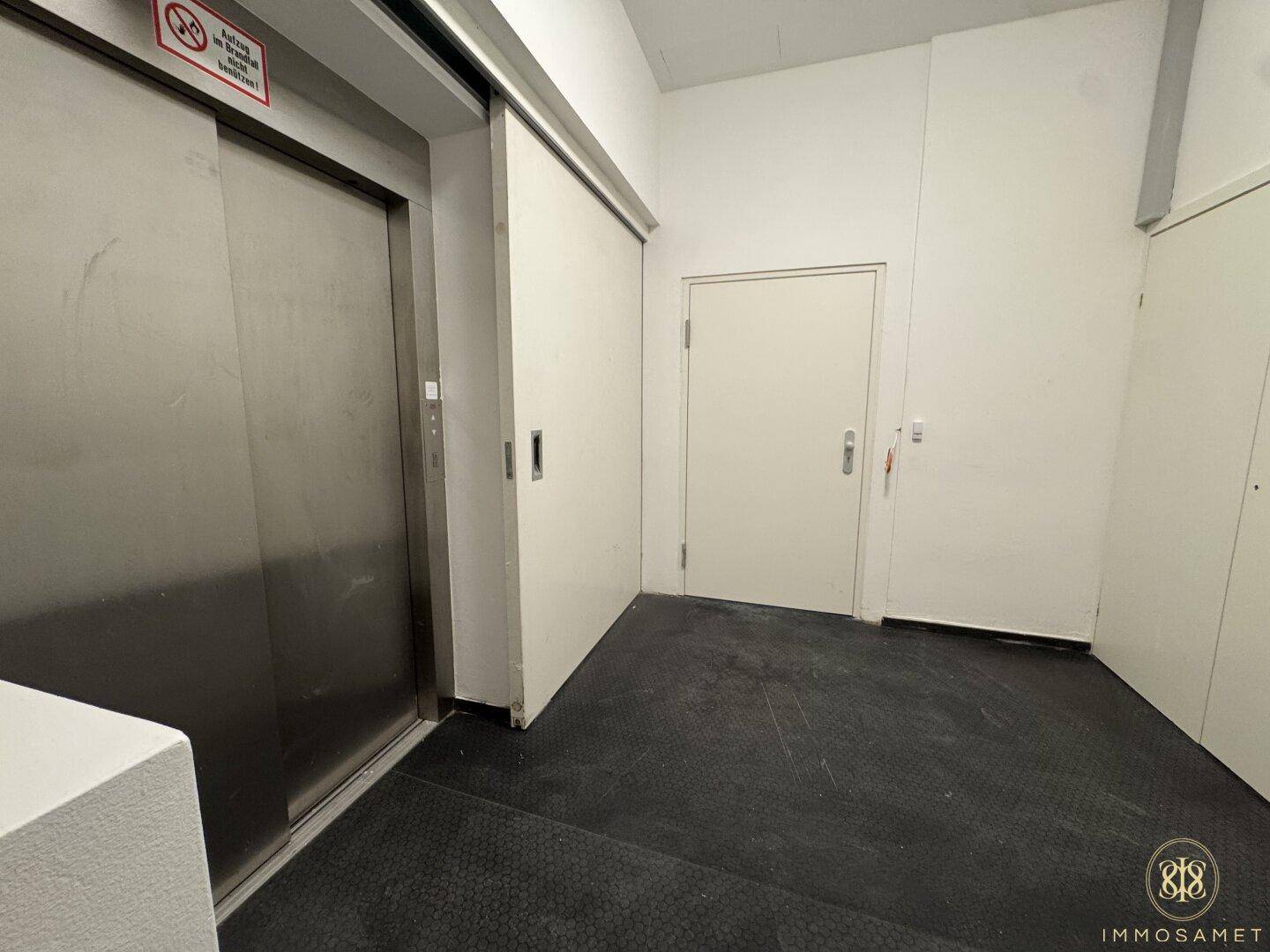 Moderner Aufzugsbereich mit Edelstahltüren und dunklem Bodenbelag, bietet bequemen Zugang zu den oberen Etagen des Gebäudes.