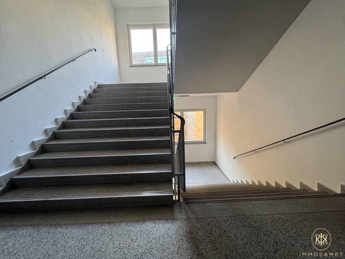 Helles Treppenhaus mit robusten Steinstufen und Handläufen, das die verschiedenen Etagen verbindet.