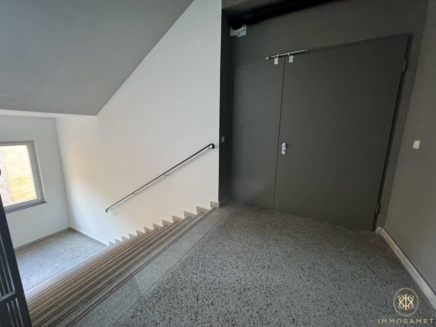 Treppenabsatz mit Steinfliesen und einer großen, dunklen Tür, die zu einem weiteren Bereich führt.