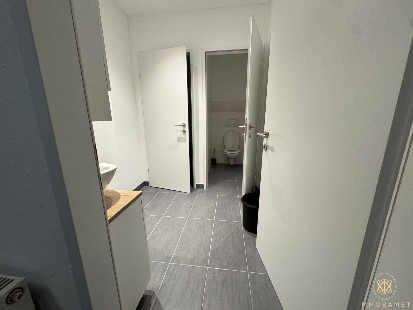 Eingangsbereich zu den Toiletten mit gefliestem Boden und einem Waschbeckenbereich im Vordergrund.