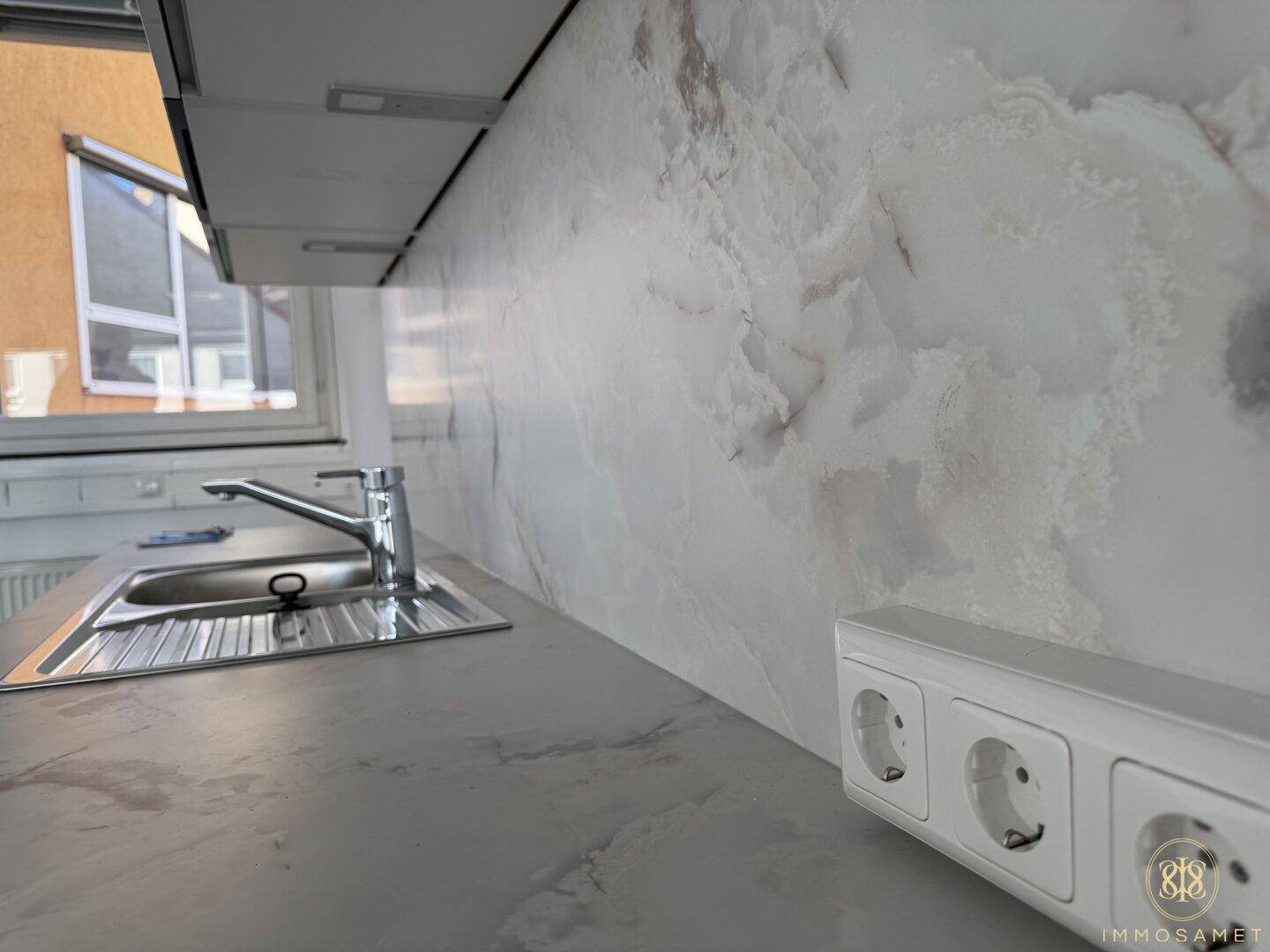 Detailansicht der Küchenzeile mit Spüle, Armatur und einer eleganten Marmor-Optik-Rückwand.