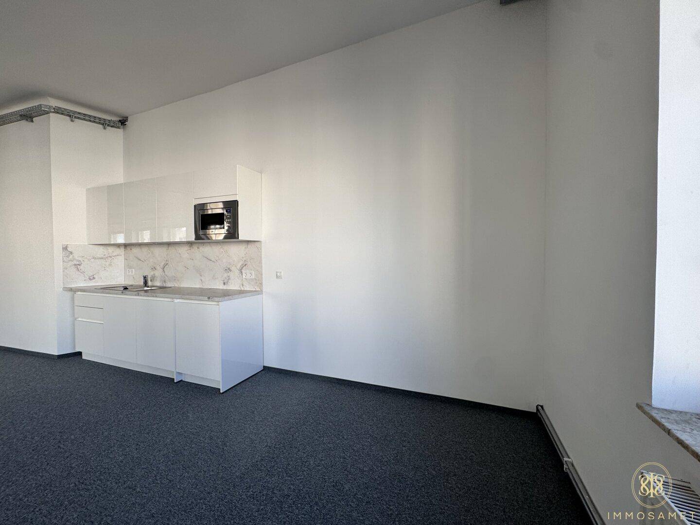 Moderne, weiße Küchenzeile mit Mikrowelle und Marmor-Rückwand in einem hellen Büroraum.