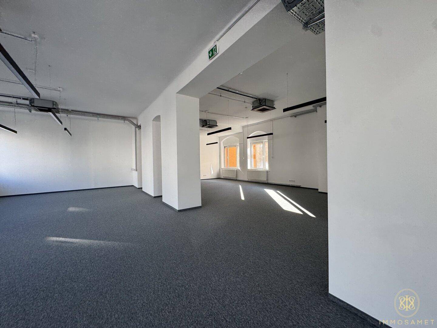 Heller, offener Bürobereich mit Teppichboden, hohen Säulen und Fenstern, die viel Tageslicht hereinlassen.