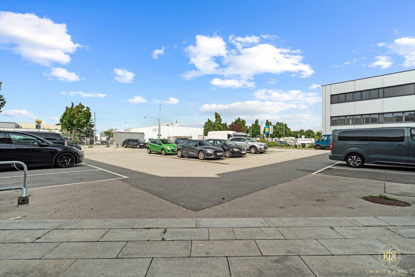 Großer Außenparkplatz mit vielen Stellplätzen unter blauem Himmel, umgeben von Geschäftsgebäuden.