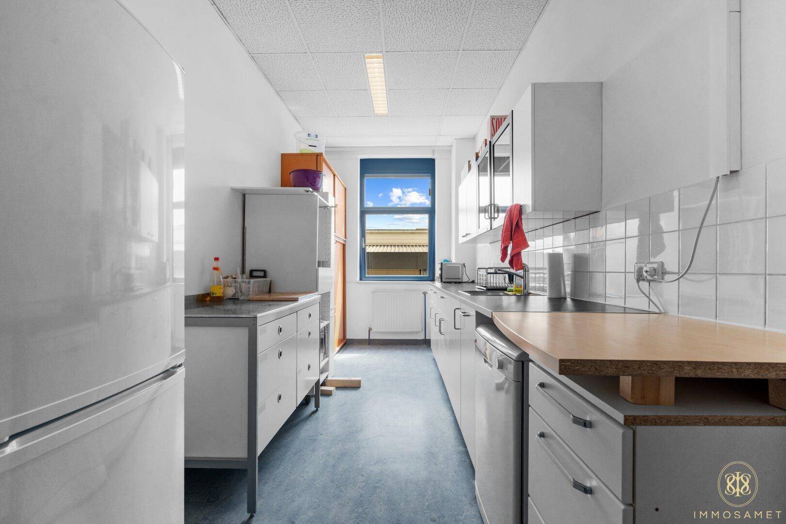 Funktionale Küche mit weißen Schränken, Fliesenrückwand und Fenster, ausgestattet mit Kühlschrank und Spülmaschine.